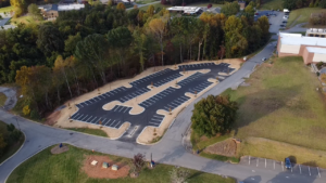 Aerial view of an empty, newly paved parking lot surrounded by trees and grass, with painted parking spaces and road access.