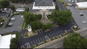 Aerial view of a large brick building with a clock tower, surrounded by landscaped greenery, parking lots, and roads.